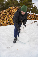 Man building snowman in winter forest with logs