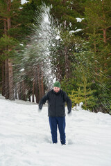Man shaking snow off tree having fun in winter forest