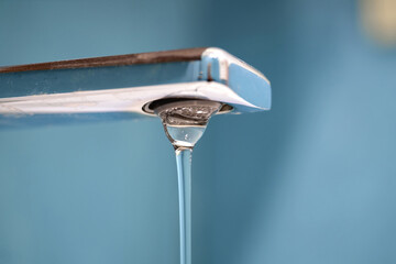 A chrome faucet with water dripping from its spout. selective focus