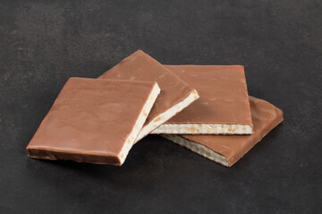 Nougat with peanuts in milk chocolate. Square shape. Dark gray background. Close-up