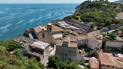 Aerial drone view of historic rooftops in an Italian coastal town with sea and cliffs nearby.