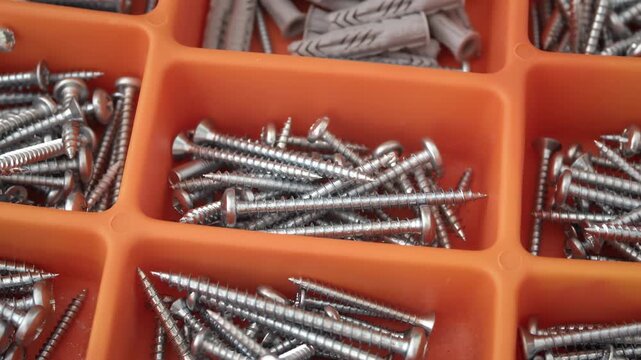 Assorted metal screws stored in orange plastic container compartments close-up