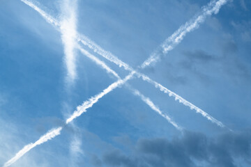 Airplane contrails crossing in blue sky with clouds