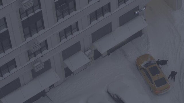 Taxi driver clearing snow from a car as a female passenger enters during heavy snowfall, natural ungraded footage, urban winter transportation