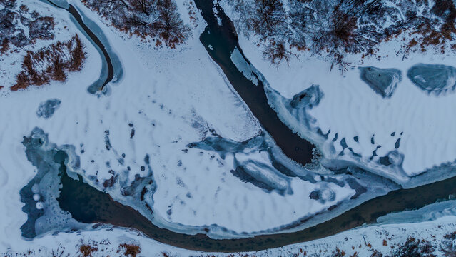 Im Winter sind Schnee und Eis &uuml;ber einem Fluss zu sehen, der durch eine verschneite Landschaft flie&szlig;t