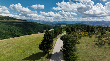Aerial drone view of a winding road through forested mountains in Italy. Natural landscape with depth and cinematic perspective.