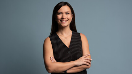 Beautiful, attractive, middle aged woman wearing casual black vest with arms crossed standing isolated on blue background