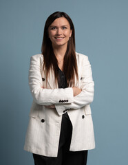 Beautiful, attractive, middle aged woman wearing casual white jacket with arms crossed standing isolated on blue background