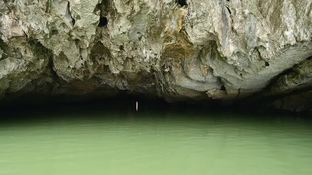 Point of view footage of a boat slowly entering a natural water cave in Tam Coc, Vietnam, one of the most iconic landscapes of Ninh Binh. The camera moves over calm river water toward a limestone 