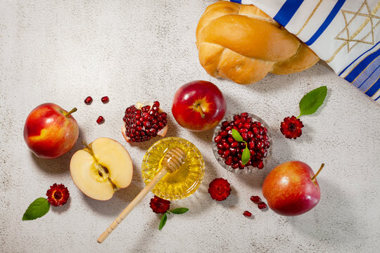 Rosh Hashanah, the Jewish New Year. Traditional symbols are tallit, apples, pomegranate, hala bread and honey on a light background. Happy Rosh Hashanah. Shana Tova.