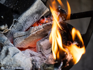 Close-up of burning wood logs and glowing hot charcoal with bright orange flames in a fire pit or barbecue.