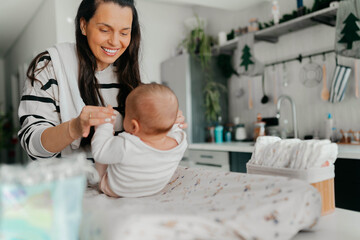 Obraz premium A smiling mother nursing her cute baby girl, holding her little legs at home.