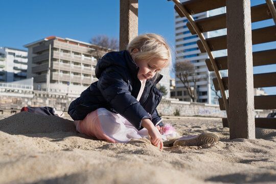 Little 4 year old girl playing on a sandy beach in Portugal during winter wearing a warm jacket.