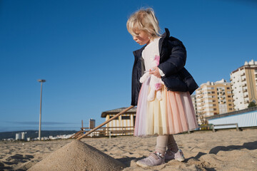 Little 4 year old girl playing on a sandy beach in Portugal during winter wearing a warm jacket.