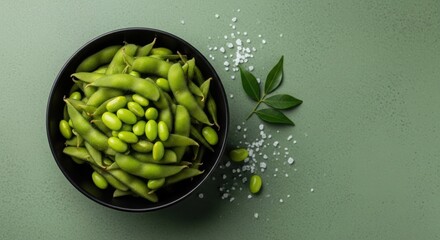 Fresh green edamame beans in a dark bowl on a sage green surface