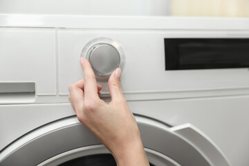 Naklejka premium Woman turning on white washing machine indoors, closeup