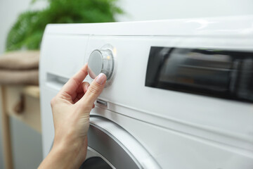 Woman turning on white washing machine indoors, closeup