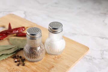 Salt and pepper shakers with condiments on white marble table, closeup. Space for text
