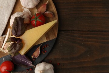 Dairy product. Piece of cheese, tomatoes, basil, peppercorns and garlic on wooden table, flat lay....