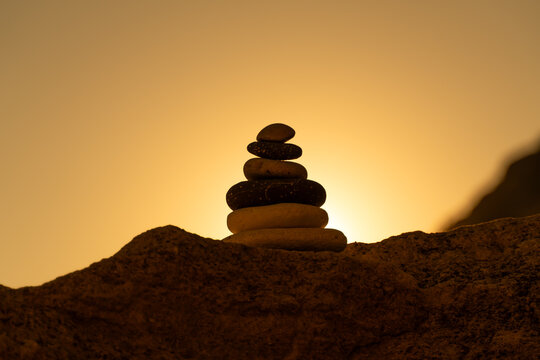 Balance cairn silhouette stacks stones against a vibrant golden sunset sky, symbolizing meditation and tranquility.