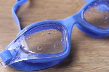 Swimming goggles with water drops on wooden table, closeup