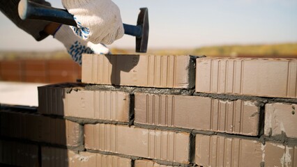 Worker building brick wall with hammer during construction