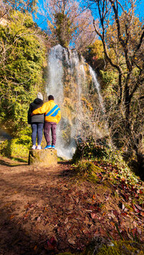 Young couple seen from behind enjoying the spectacular view of the Fuentetoba waterfall in Soria. A perfect scene of hiking, adventure, and romantic travel in a beautiful natural park.
