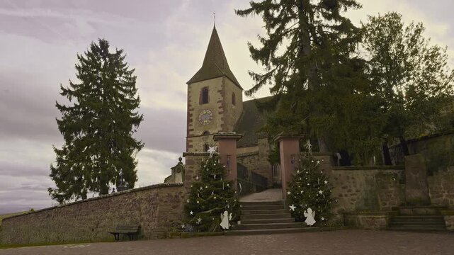 Entrance with Christmas trees to the complex consisting of an ancient fortified church serving both Catholic and Protestant rites, and its cemetery, in Hunawhir, Alsace.