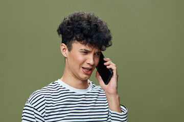 young man talking on smartphone with striped shirt, curly hair, casual style, olive green background, expressive facial expression, communication concept
