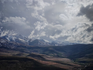 A landscape in the Caucasus Mountains on a cloudy day, a panoramic view with snow in the mountains and wooded areas