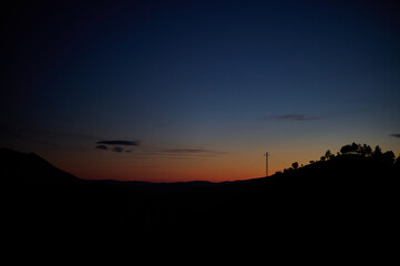 Fototapeta premium Silhouette of a hill with trees and electric pole against a deep blue and orange twilight sky at sunset in Pyrenees