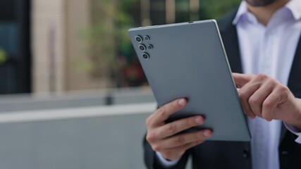 Crop view of young businessman hand holds digital tablet on modern city street. Business professional uses mobile device for communication and data analytics in financial district - Powered by Adobe
