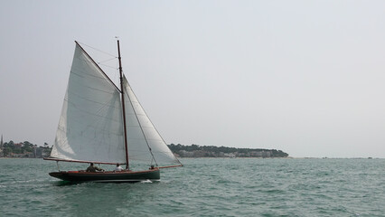 Fototapeta premium Voilier traditionnel en bois naviguant sur une mer calme avec voiles blanches