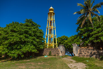 Historic El Faro lighthouse in Puerto Plata, Dominican Republic, viewed from below on a sunny day, with blue sky, green trees and iconic iron structure symbolizing Caribbean heritage
