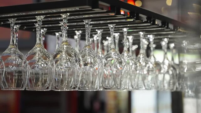 Neatly arranged rows of inverted wine glasses hanging from a metal rack in a contemporary bar interior, shimmering with reflections and bokeh lights for a elegant atmosphere.