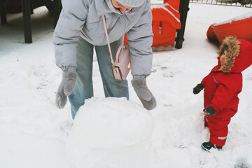 Child Building Snowball with Adult in Winter Park