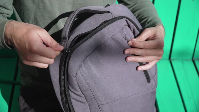 Diverging backpack zipper in hands of Caucasian man as he attempts to close it closeup. Unforeseen inconvenience caused by wear of clothing hardware and accessories for laptops and travel.