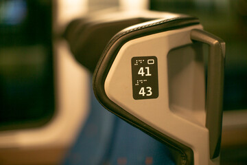 Closeup seat armrest number plaque embossed digits , textured plastic finish and backrest edge, blue upholstery blurred background, reserved seating context suggesting