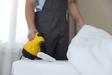 Pest control worker cleaning bed with steam cleaner indoors, closeup
