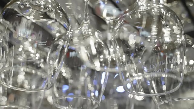 Rows of inverted glassware hanging from an overhead rack in a bar setting, sparkling under ambient lights with shimmering bokeh reflections, clean polished stemware for service