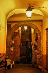 Illuminated by lanterns, an arched passage in an old Italian courtyard with flowerpot decor and stairs