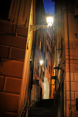 Narrow alley with warm lantern light with stairs leading to a street with an arch and traditional facades of Mediterranean houses, Camogli, Italy