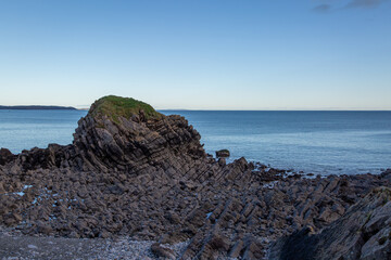 A rugged, ancient rocky coastline near Pembroke, Wales. Featuring dramatic cliffs and blue ocean waters, this scenic view captures the wild, natural beauty of the Pembrokeshire coast