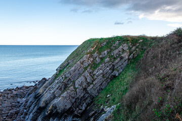 A rugged, ancient rocky coastline near Pembroke, Wales. Featuring dramatic cliffs and blue ocean waters, this scenic view captures the wild, natural beauty of the Pembrokeshire coast