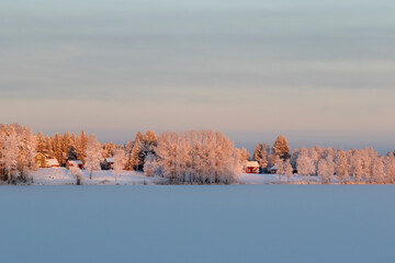 Sammakko village. Village houses and snow-covered trees on the shore of a frozen lake. 