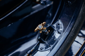 Close-up of vintage car wheel with brass nut on polished black rim