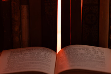 An open book with pages illuminated by a bright light source, filtering through a gap between books on a shelf. 