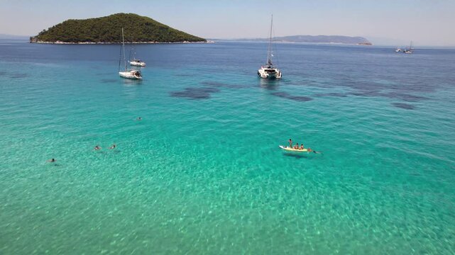 Aerial drone flyover yachts and SUP boarder towards Dassia Island Skopelos Greece 4K