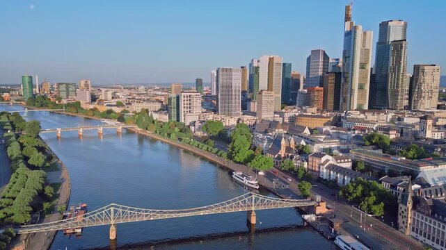 Aerial drone panning shot from Frankfurt Cathedral to the skyscraper skyline and Eiserner Steg bridge. 100m high panoramic view over the Main River and financial district in Frankfurt, Germany.