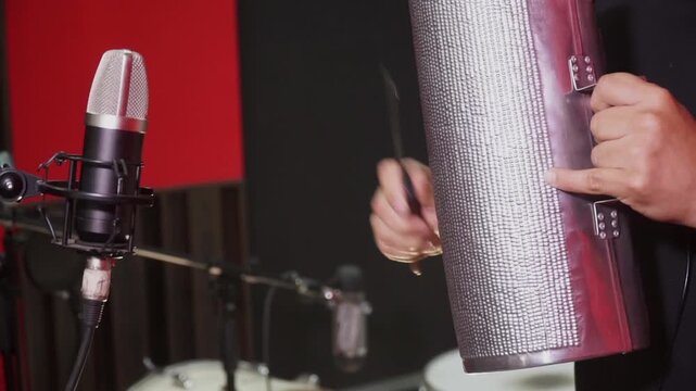 Musician playing a metal guiro in a recording studio with a professional studio microphone.
